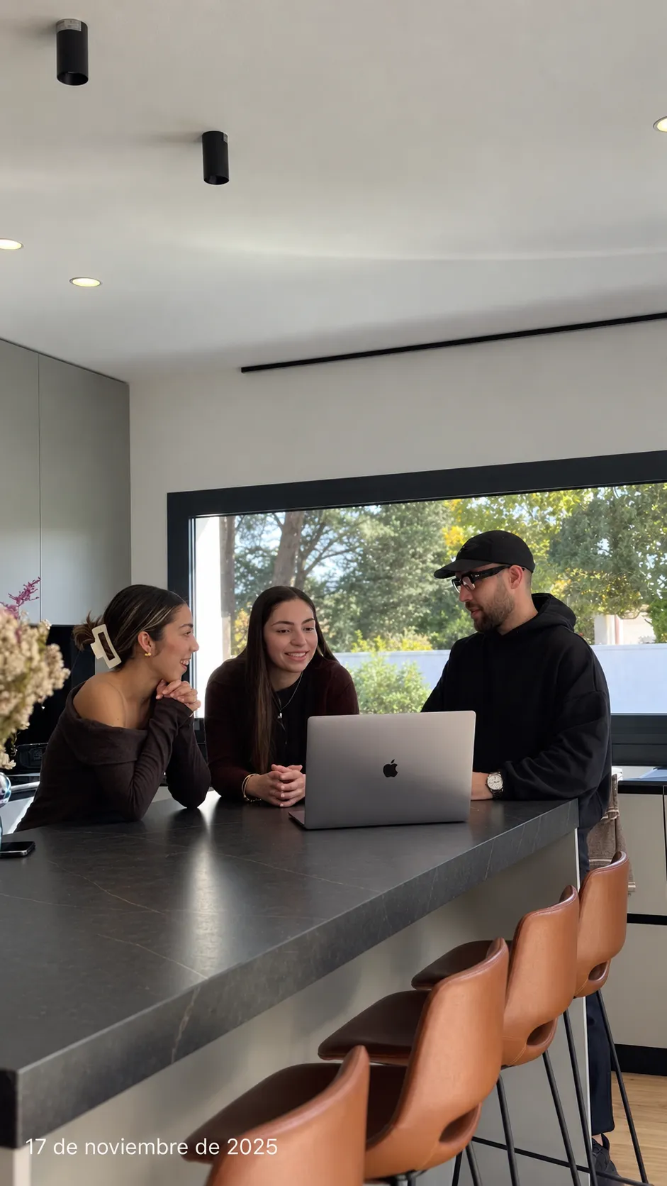 Tres personas jóvenes conversando alrededor de un portátil en una cocina